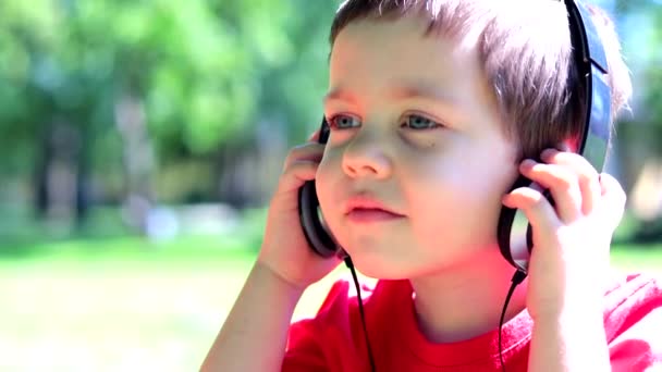 A boy with headphones listening to music on the street . Relax. Outdoor recreation. The music in the headphones. A child listens to a fairy tale in headphones. — Stock Video