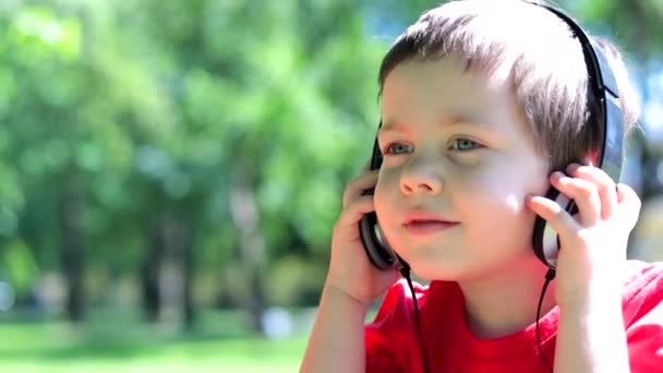 A boy with headphones listening to music on the street . Relax. Outdoor recreation. The music in the headphones. A child listens to a fairy tale in headphones. — Stock Video