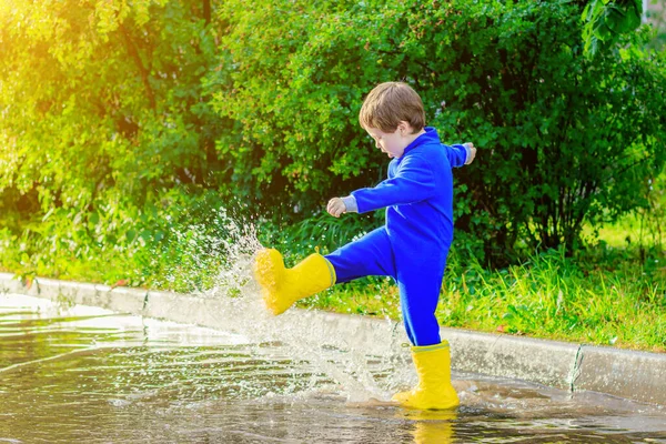 A happy boy in rubber boots jumps in puddles. The boy jumps in a puddle . Bad weather. puddles after rain. Childhood. A child in rubber boots. Summer walk. Happy child.