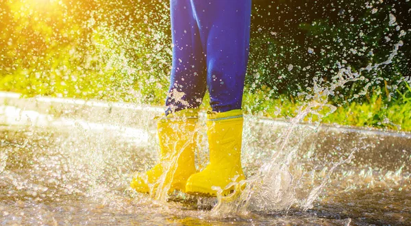 My rubber-booted feet are Bouncing in a puddle. Article about rubber boots. Children's summer shoes. Puddles after rain. Bad weather. A child jumps in a puddle. A happy boy in rubber boots jumps in puddles.