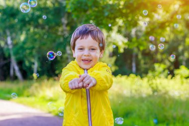 Çocuk sabun köpüklerini elleriyle yakalıyor. Erkek ve sabun köpükleri. Renkli baloncuklar. Mutlu bir çocukluk. Şehirde yaz mevsimi. Çocuk eğlencesi. Çocukların boş vakitleri kavramı. Çocukların duyguları.