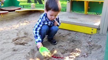 Çocuk kum havuzunu kazıyor. Sokakta oyunlar. Çocukların boş vakitleri. Kumda bir çocuk.