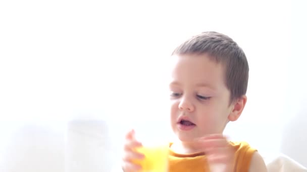 Chłopak pije sok ze szklanki. Dzieci piją. Żółty sok w szklance. — Wideo stockowe