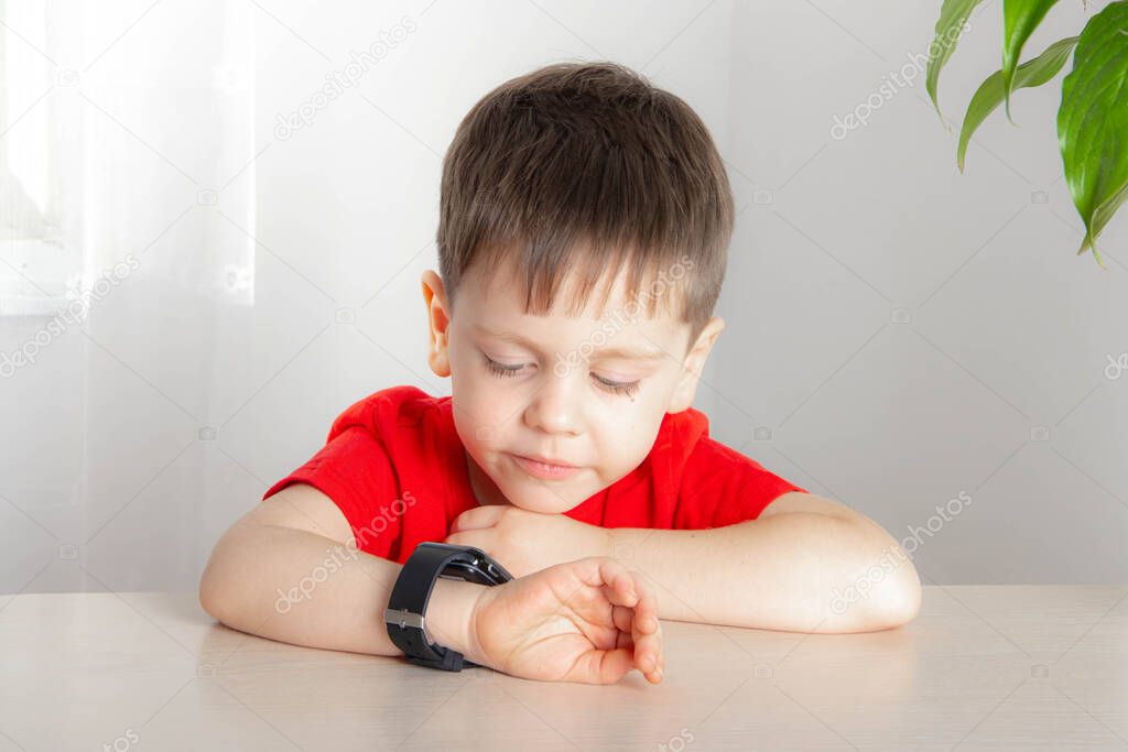 The boy looks at the time on the clock . A child is sitting at the table. An article about the time. The end of the course.