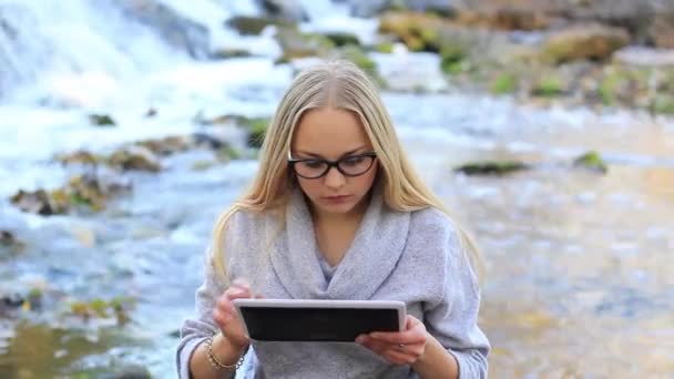 Hermosa chica cerca de la cascada con una tableta — Vídeo de stock