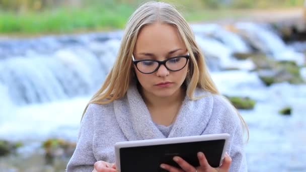 Hermosa chica cerca de la cascada con una tableta — Vídeo de stock