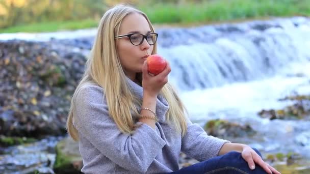 Flicka äter ett äpple nära ett vattenfall — Stockvideo