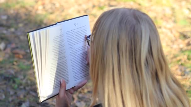 Schönes Mädchen mit Brille liest ein Buch im Wald — Stockvideo