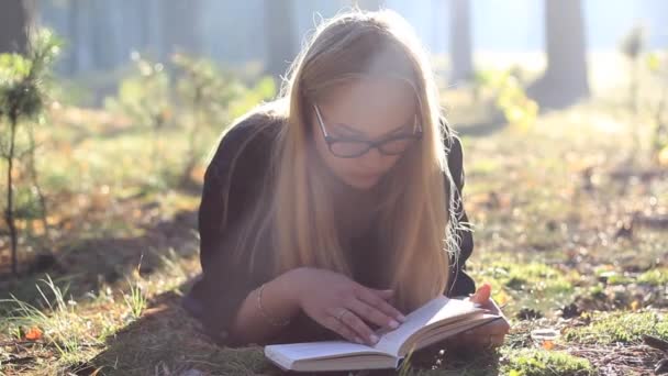 Hermosa chica en gafas leyendo un libro en el bosque — Vídeos de Stock