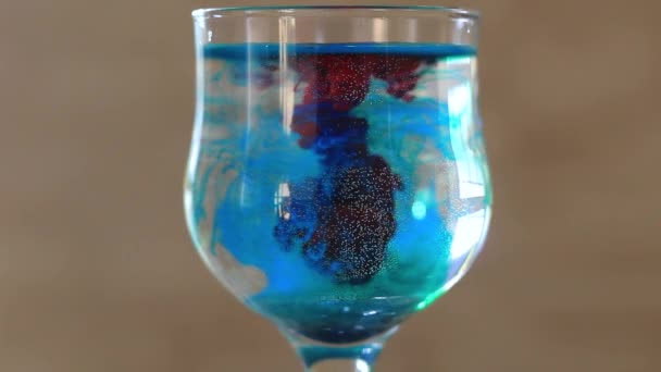 Glas mit Wasser mit roter und blauer Farbe. — Stockvideo