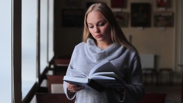 Девушка в библиотеке читает книгу — стоковое видео