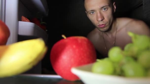 Хлопець бере фрукти з холодильника вночі — стокове відео