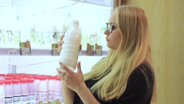 Mädchen erwägt eine Flasche Milch im Supermarkt — Stockvideo