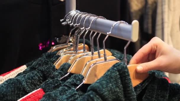 Жінка вибирає пастельні теплі затишні светри на вішалках — стокове відео
