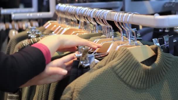 Woman choosing pastel warm cozy sweaters on hangers — Stock Video