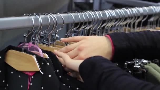 As mãos femininas no toque um cabide de casaco com a roupa na butique . — Vídeo de Stock