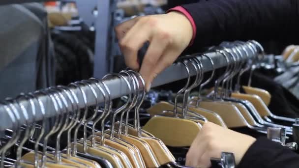 Las manos femeninas tocan una percha con ropa en boutique . — Vídeo de stock