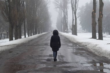 Kız yalnız ıslak bir yolda gider. arka görünüm