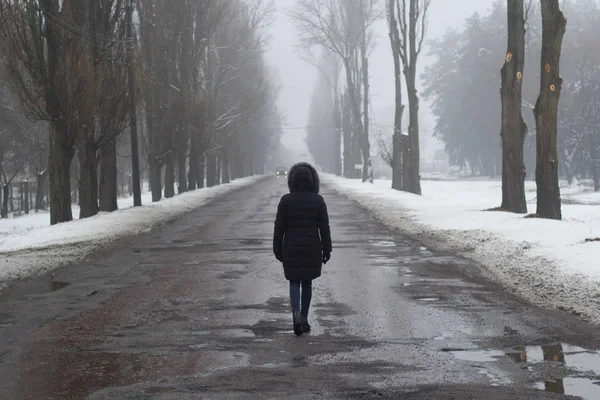 Fata merge pe un drum umed singur. vedere din spate Imagine de stoc