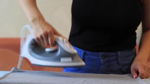 Дівчина прасує одяг з праскою на прасувальній дошці — стокове відео