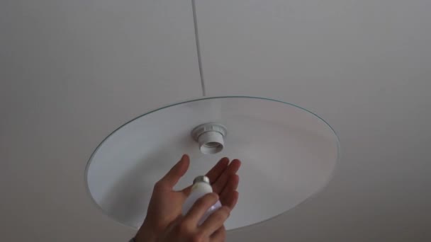 Рука человека вкручивает лампочку в люстру на кухне — стоковое видео