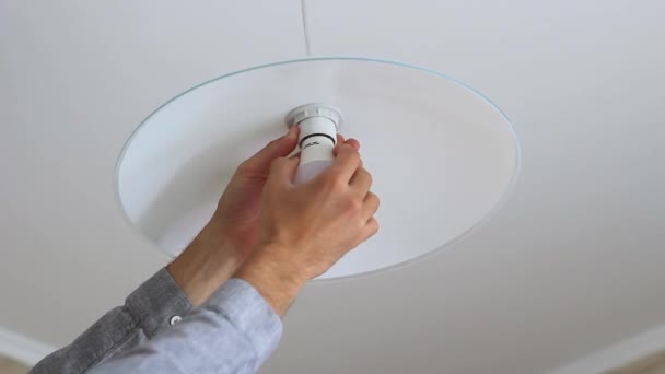 A mans hand is screwing an light bulb into a chandelier in the kitchen — Stock Video