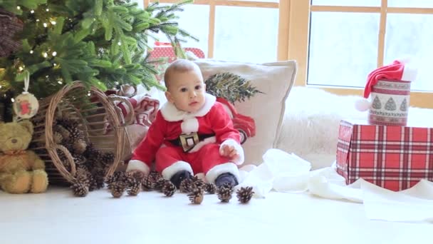 Kleine baby zittend op de vloer in de kamer voor een versierde kerstboom — Stockvideo
