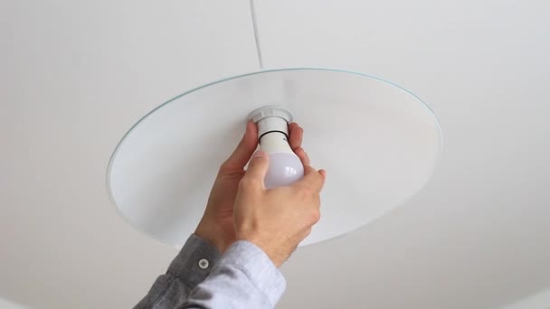 Close-up of male hand twists LED lamp into ceiling light . — Stock Video