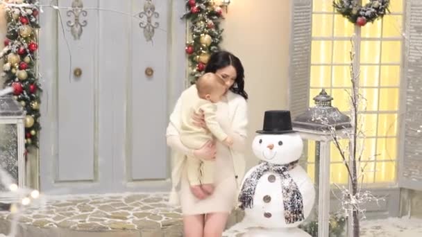 Joven madre y su pequeño bebé con un muñeco de nieve en Navidad — Vídeos de Stock