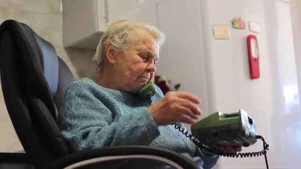 회색 머리 할머니 가 집에 있는 리모 콘으로 전화를 걸어 이야기하는 모습 — 비디오