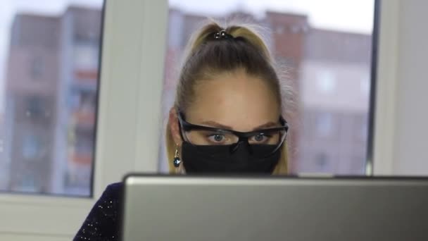 Dívka na volné noze pracuje na notebooku během epidemie koronoviru v lékařské masce a brýlích.