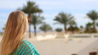 Denizde tatil. Genç güzel kız güneş gözlüklü palmiye ağaçlarına bakar, arkadan bakar..