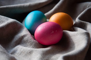 Paskalya yumurtaları gri keten kumaş kıvrımları ile pembe turuncu renk mavi. Yan ve üst görüntüleme.