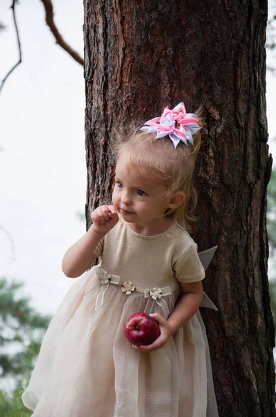 Pequena menina bonita brincando na natureza na floresta. A criança está sorrindo e segurando uma maçã vermelha — Fotografia de Stock