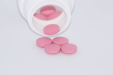 Beyaz arka plan üzerinde pembe hap plastik bir kavanozdan düşmek