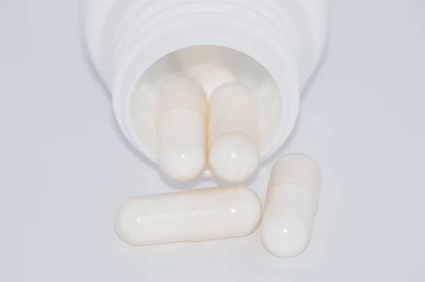 Pillole bianche su sfondo bianco cadono da un barattolo di plastica . — Foto Stock