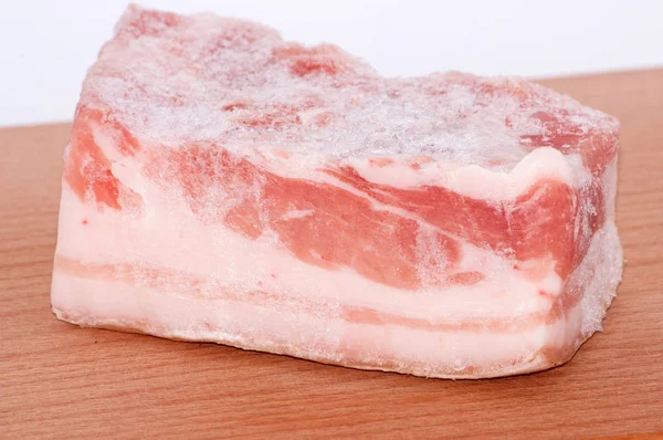 Grande pezzo di pancetta di maiale congelata su un tagliere — Foto Stock