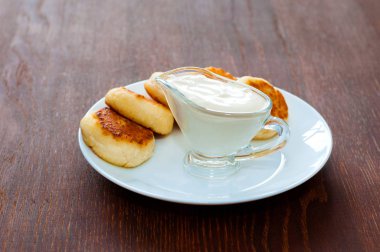 Koyu ahşap bir masa üzerinde beyaz bir tabak üzerinde ekşi krema ile Cheesecakes, arka plan