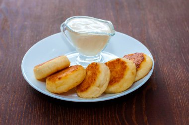 Koyu ahşap bir masa üzerinde beyaz bir tabak üzerinde ekşi krema ile kızarmış peynir krep. Kafe veya restoran menü tasarımı için.