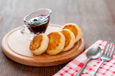 Ahşap tahta tahta lar üzerinde kuş üzümü reçeli ile Peynir Pancake, bir çatal, kaşık ve mutfak havlusu ile