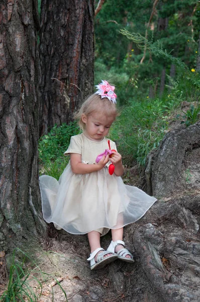 Petite belle fille jouant dans la nature dans la forêt. Assis sous un arbre et regarde le ballon et les cœurs — Photo