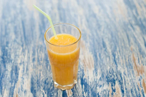 Orange juice in a glass with a straw on a blue wooden background of sea-green close-up — Stock Photo, Image