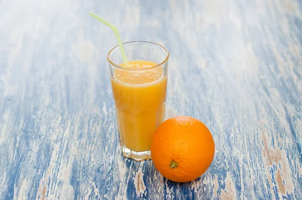 Glass of juice with straw and orange on a blue background — Stock Photo, Image