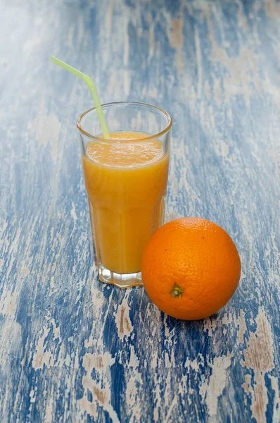 Glass of juice with straw and orange on a blue background — Stock Photo, Image