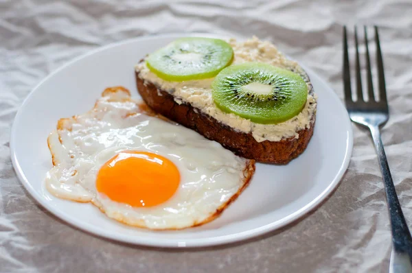 Delicioso e saudável café da manhã. Ovos fritos e sanduíche de kiwi na placa branca — Fotografia de Stock