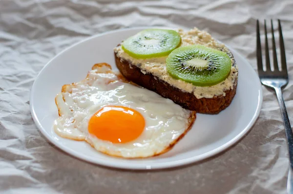 Pyszne i zdrowe śniadanie. Jajka smażone i kanapka z kiwi na białej płycie — Zdjęcie stockowe