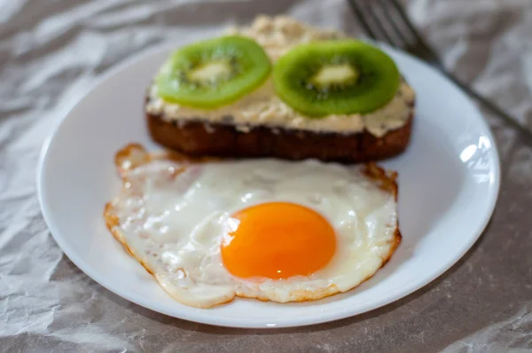 Delicious and healthy breakfast. Fried eggs and kiwi sandwich on a white plate, close-up, space for text — Stock Photo, Image