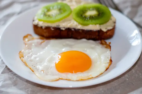 Heerlijk en gezond ontbijt. Gebakken eieren en kiwi sandwich op een witte plaat, close-up, ruimte voor tekst — Stockfoto