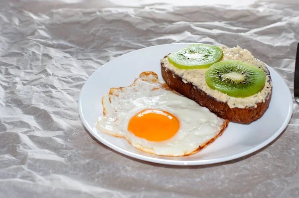 Delicioso e saudável café da manhã. Ovos fritos e sanduíche de kiwi em um prato branco, close-up, espaço para texto — Fotografia de Stock