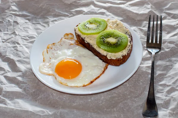 Delicioso y saludable desayuno. Huevos fritos y sándwich de kiwi en un plato blanco, primer plano, espacio para el texto — Foto de Stock